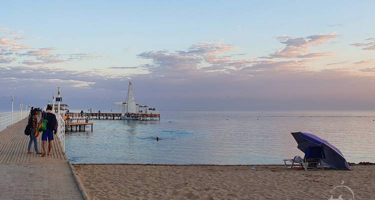 A beach scene with people walking on a pier and a calm sea.
