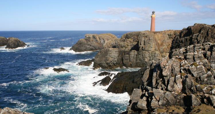 Falaises rocheuses battues par les vagues avec un phare solitaire se dressant au-dessus de l'Atlantique.