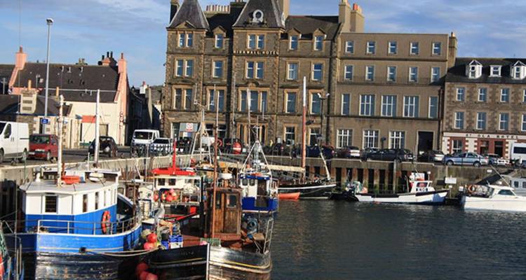 Des bateaux de pêche amarrés près de bâtiments traditionnels en pierre dans un petit port de ville.