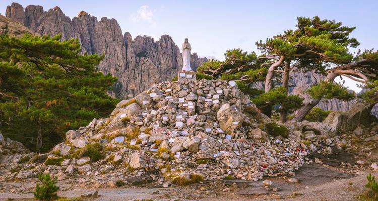 A statue surrounded by rugged rocks and twisted trees, with dramatic cliffs in the background.