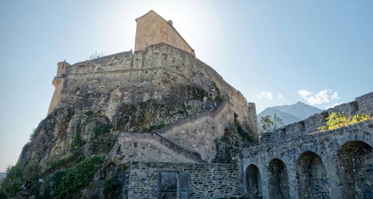 An ancient stone fortification with detailed architecture, shot from below with sunlight