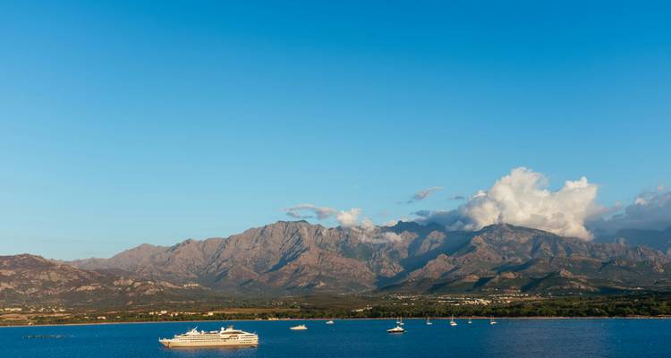 A view of boats on the water with mountains in the background under a clear blue sky.