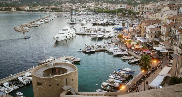 A lively harbor scene with boats, a tower, and people along the waterfront.
