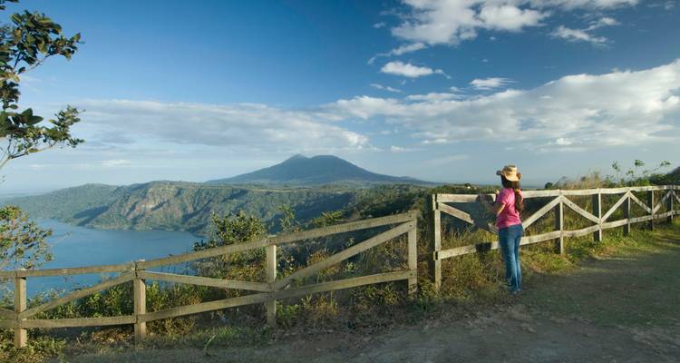 A woman enjoys a panoramic view of a volcanic lake and mountains.