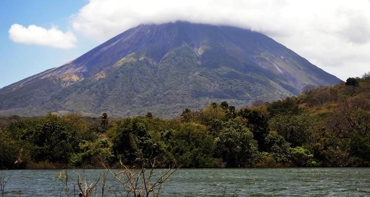 A large volcano partially covered by clouds viewed across a lake.