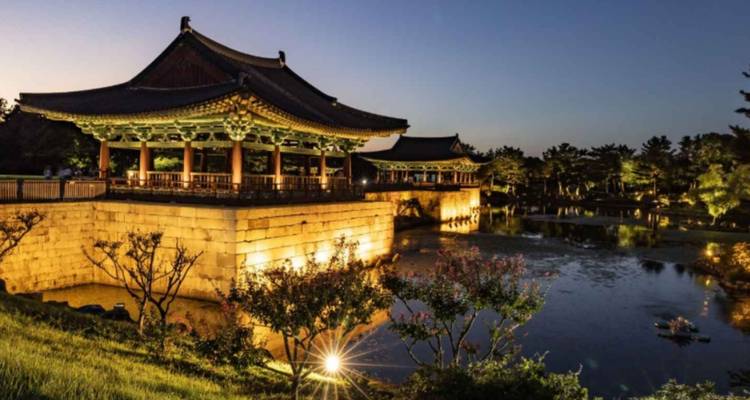 Pavillon coréen traditionnel illuminé la nuit au bord d'un étang.