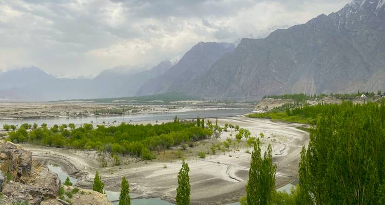 Large vallée avec rivière en tresses, bancs de sable et verdure printanière fraîche sous des pics escarpés.