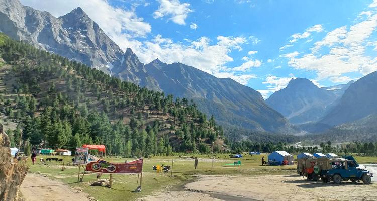 Campement de montagne avec tentes, forêts de pins et pics spectaculaires du Karakoram sous un ciel lumineux