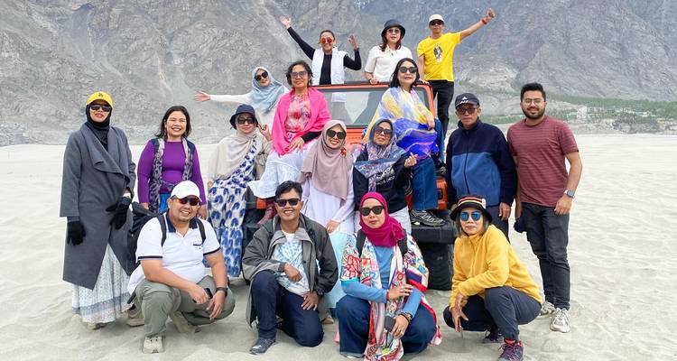 Groupe de touristes excités posant près d'un véhicule tout-terrain sur du sable pâle et large avec des montagnes escarpées en arrière-plan