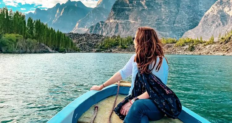 Femme assise à la proue d'un bateau bleu sur un lac alpin tranquille entouré de pics spectaculaires