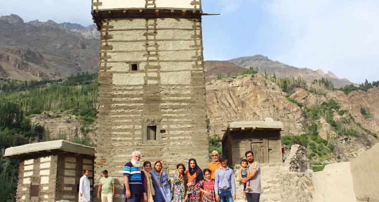 Grupo familiar posando frente a una antigua torre de vigilancia de piedra y un paisaje montañoso escarpado en Hunza.