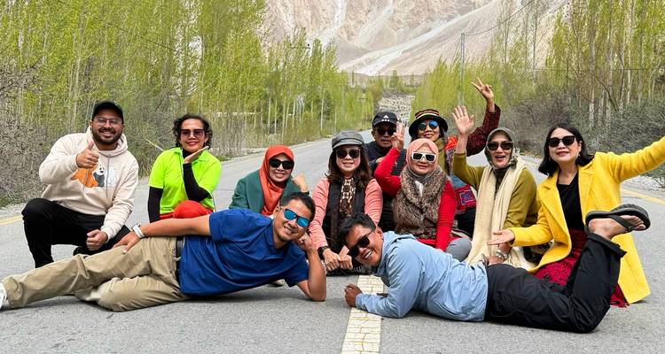 Grupo alegre de viajeros posa acostado a lo largo de una carretera de montaña bordeada de álamos altos en el Valle de Hunza