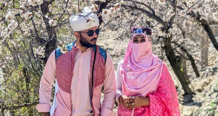 Pareja con vestimenta tradicional de pie bajo flores de albaricoque en flor en el norte de Pakistán