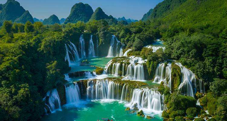 Spectacular multi-tiered turquoise waterfall surrounded by dense green jungle and limestone peaks.