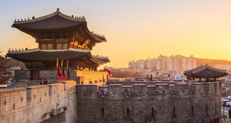 A traditional Korean gate with a cityscape during sunset.