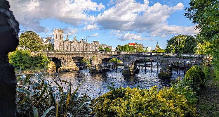 Malerische Aussicht auf eine Brücke über einen Fluss mit üppigem Grün und einer Kirche.