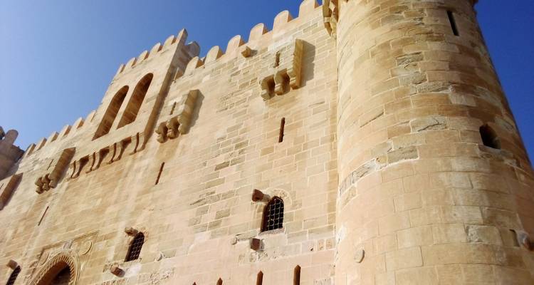 Ancienne forteresse avec des murs de pierre et des tours sous un ciel bleu clair.