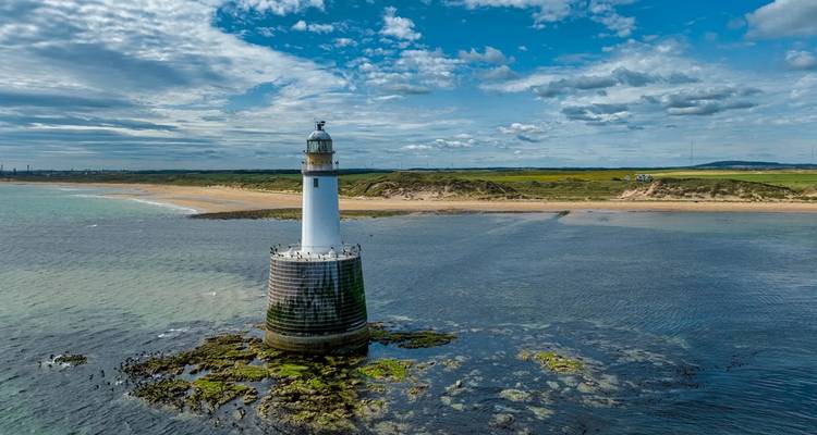 Phare en mer avec un arrière-plan de plages de sable et de ciel bleu.