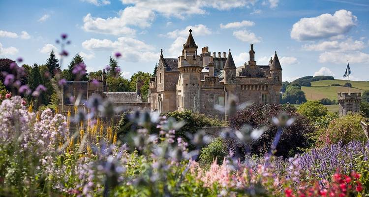 Château entouré de jardins de fleurs colorés, avec un ciel bleu clair.