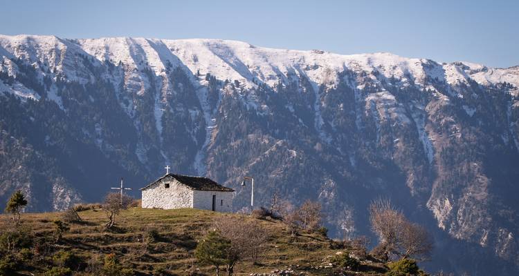 Petite chapelle avec une croix sur une colline avec des montagnes enneigées en arrière-plan.
