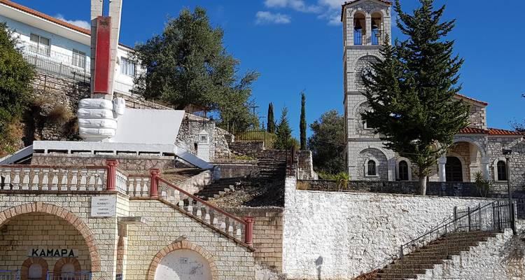 Église en pierre avec clocher et une sculpture de main au premier plan.