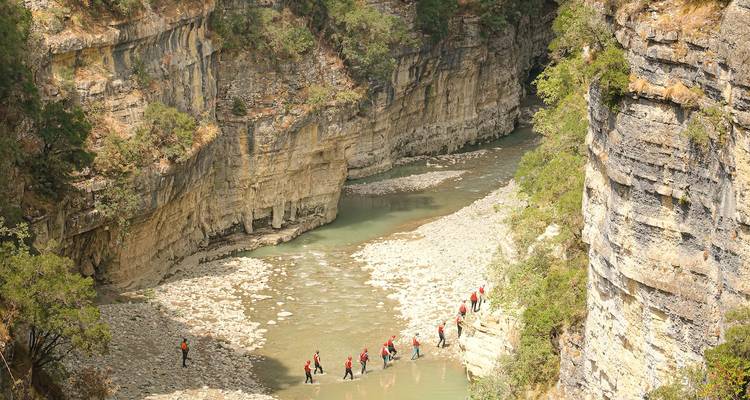 Des personnes marchent le long d'une rivière dans une gorge, entourées de hautes parois rocheuses.