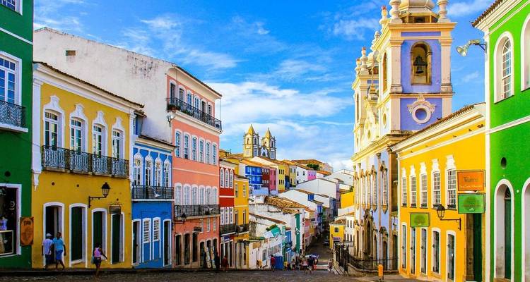 Vibrant colonial street with colorful buildings, blue sky, and church towers.