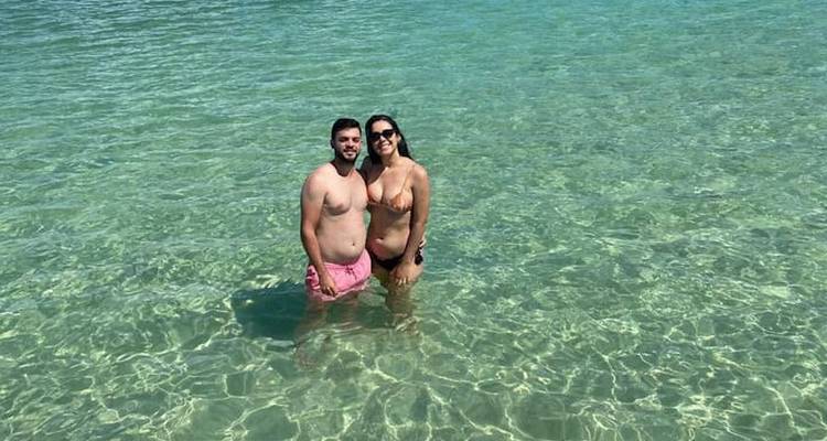 Couple standing in clear, shallow ocean water on a sunny day.