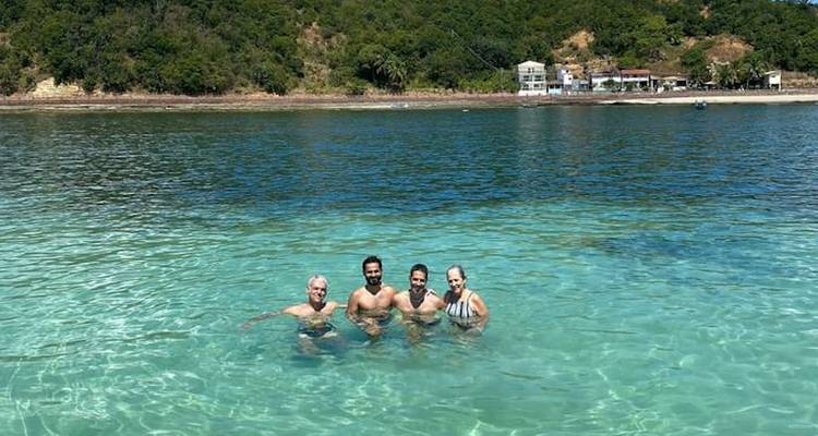 Group of four adults swimming in clear ocean water with a beach in the background.