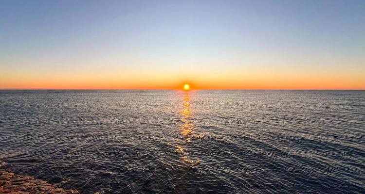 Atardecer sobre el océano reflejando el resplandor naranja en el agua.