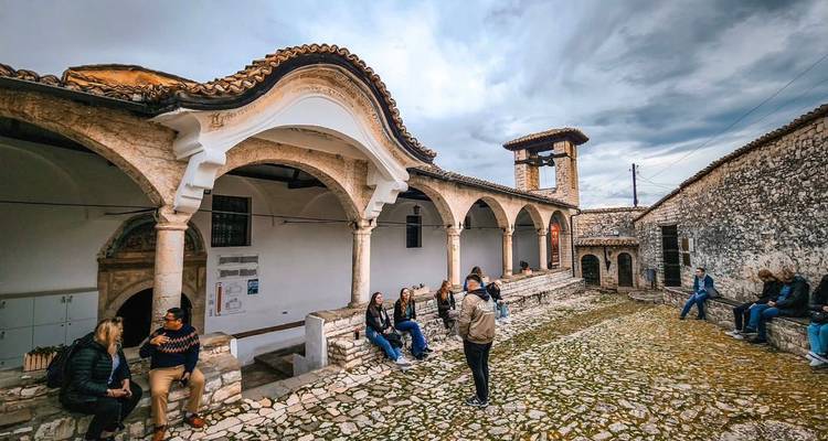 Personas sentadas en un patio histórico con arcos y campanario.