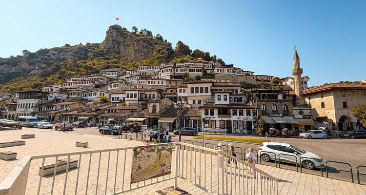 Vista de calle con casas en ladera y torre de mezquita bajo un cielo despejado.