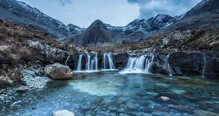 Une chaîne de montagnes avec une petite cascade qui se déverse dans un bassin limpide.