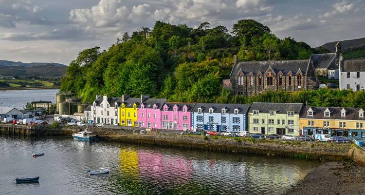 Maisons colorées au bord de l'eau avec une colline boisée en arrière-plan.