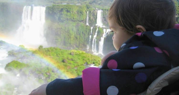 Child looking at a waterfall with a visible rainbow.