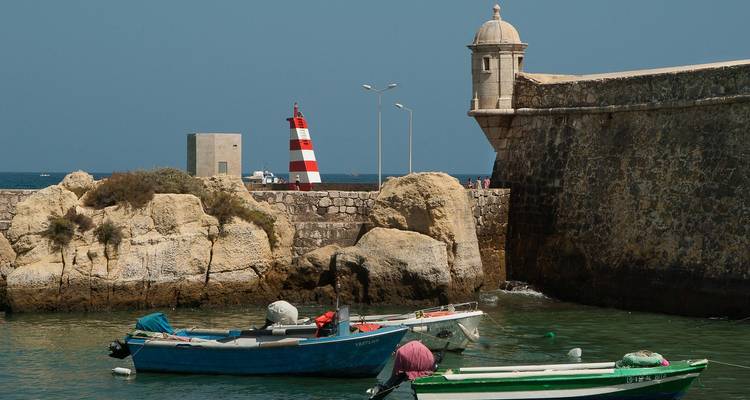 Côte rocheuse avec des bateaux et un phare à rayures rouges.