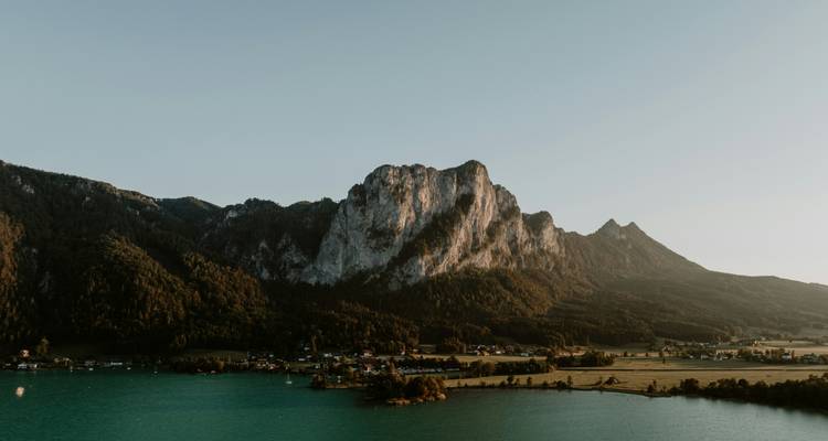 Uitzicht op bergen over een serene meer met een zachte zonsonderganggloed.