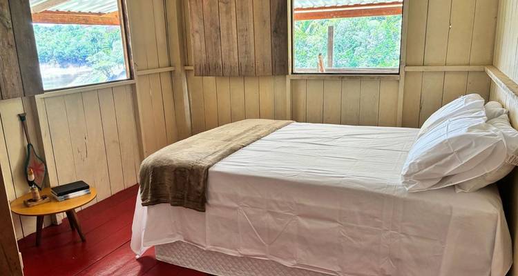 Intérieur d'une chambre simple avec un lit, deux fenêtres montrant de la verdure extérieure.