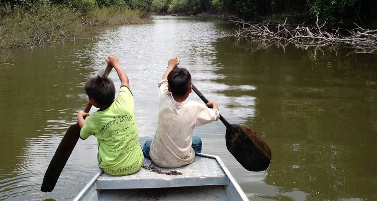 Deux enfants pagayant à travers une voie navigable entourée d'une végétation luxuriante.