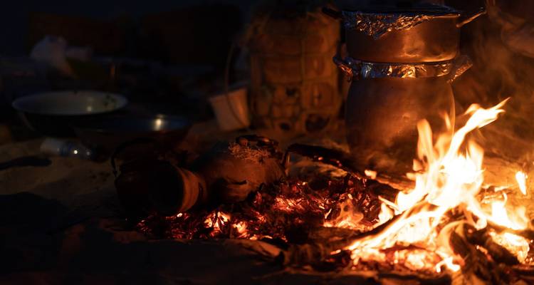 A campfire with cooking pots and are near it.