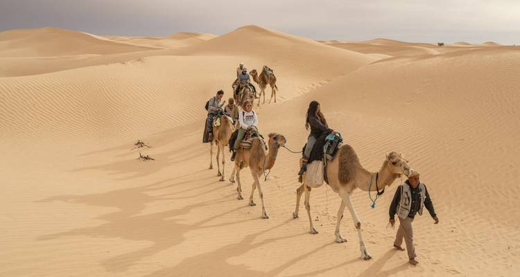 People riding camels in the desert.