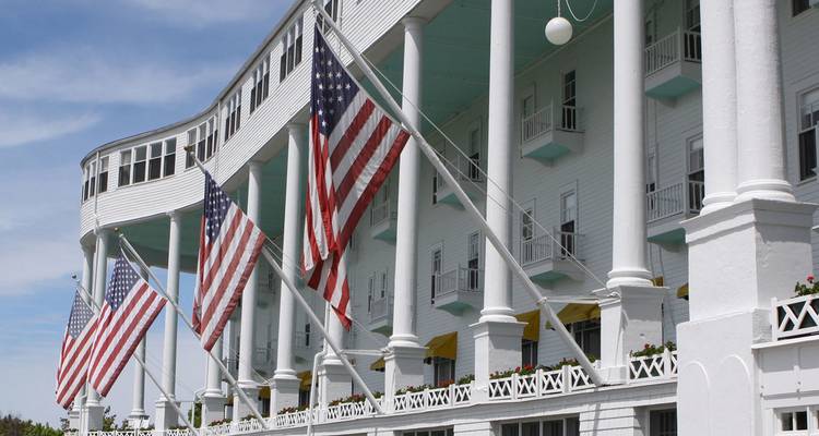 La fachada de columnas blancas del Grand Hotel en la Isla Mackinac está adornada con grandes banderas estadounidenses en un día soleado.