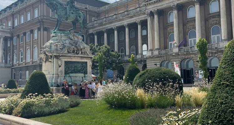 Des gens se sont rassemblés près d'une statue devant un grand bâtiment avec des jardins.
