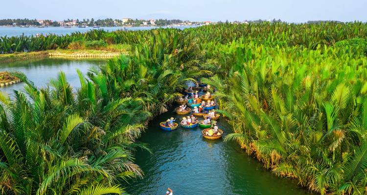 Rivière serpentant à travers un paysage verdoyant luxuriant avec des personnes dans des bateaux ronds.