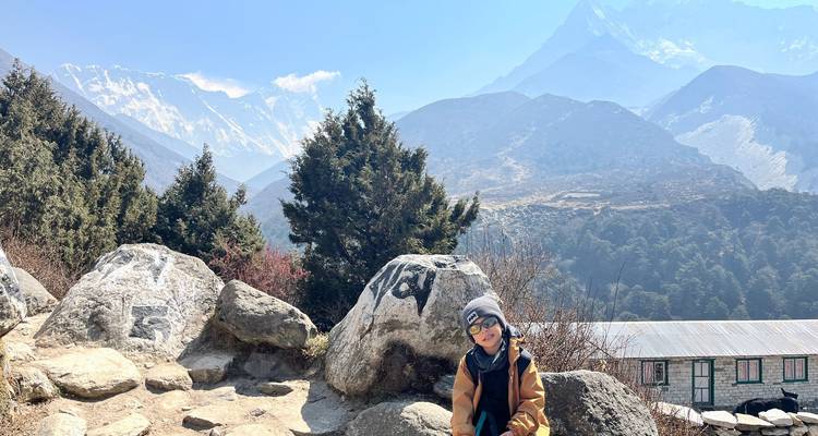 Une femme assise sur des rochers avec une vue sur l'Himalaya.