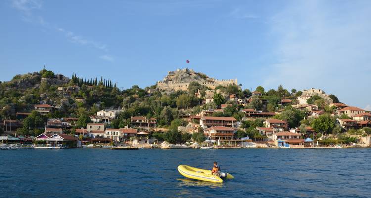 Village côtier avec forteresse en pierre sur la colline ; personne en kayak.
