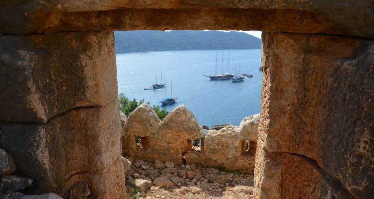 Vue à travers une arche de pierre ancienne vers une baie avec des bateaux.