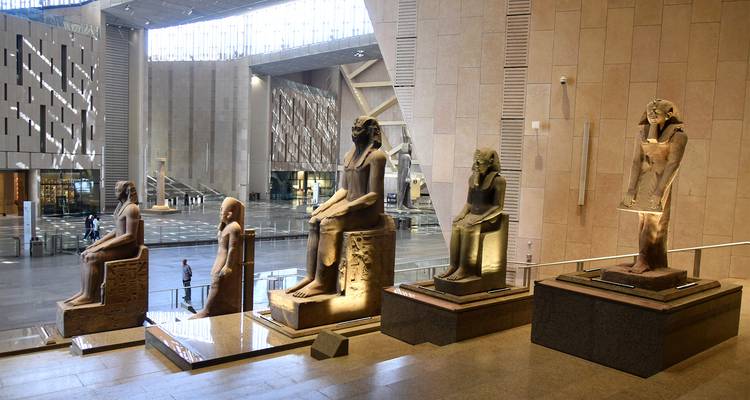 À l'intérieur d'un musée, des statues égyptiennes antiques exposées avec des visiteurs autour.