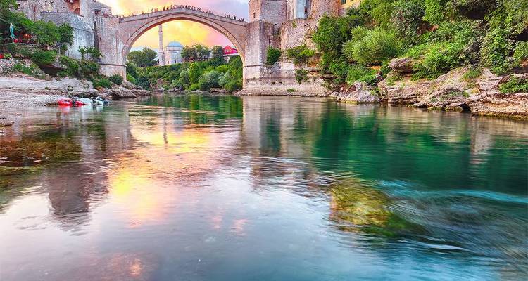 Vieux pont au-dessus d'une rivière avec un environnement luxuriant au coucher du soleil.
