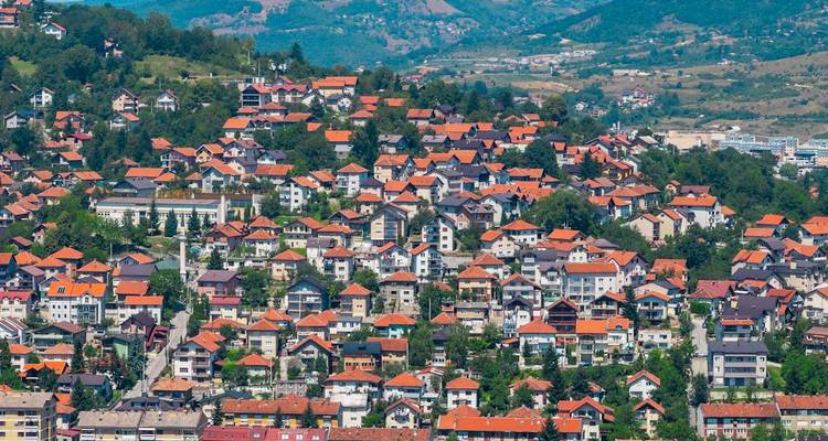 Maisons aux toits rouges sur une colline avec un décor naturel en arrière-plan.